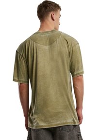 Olivově zelené oversized tričko s měkkým, texturovaným povrchem. Krátké rukávy a zaoblený výstřih. Oblečení se vzorem z vybledlé, nepravidelné barvy.