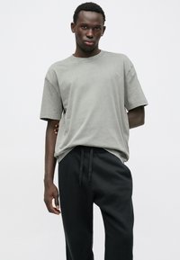 Γκρι βαμβακερό t-shirt με κοντά μανίκια και χαλαρή εφαρμογή, συνδυασμένο με μαύρες φόρμες που διαθέτουν ελαστική μέση και κορδόνια.