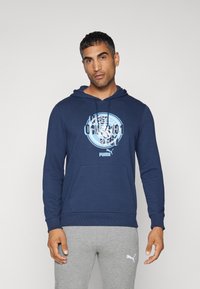 Felpa blu navy con una stampa grafica circolare in azzurro chiaro centrata sul petto, dotata di tasca a marsupio e cappuccio con coulisse regolabile.