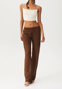 Pantalons en tricot texturé marron avec une coupe décontractée et une taille élastique, associés à un haut court blanc ajusté à fines bretelles.