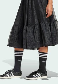 Black ruffled skirt with a shimmering texture paired with black and white striped Adidas socks and black textured sneakers.