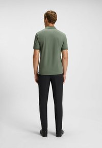 Kortärmad olivgrön polo-shirt, slät textur, detaljerad krage. I kombination med svarta byxor, slim fit, och svarta skor.