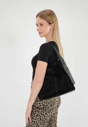 Zwarte suède handtas met een gestructureerde zwarte leren schouderriem. Heeft een slouchy ontwerp en gouden hardware-accenten. Zachte, matte afwerking.