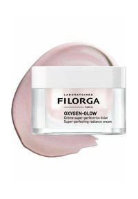 Filorga Oxygen-Glow cream in a clear jar features a white lid. A pink cream is swatched alongside, showcasing its smooth, creamy texture.