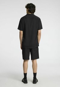 Set composto da una maglietta nera a maniche corte e pantaloni corti, realizzato in tessuto liscio. Presenta un colletto standard e una vestibilità rilassata. Calzini e scarpe neri completano il look.
