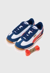 Kék, fehér és piros szintetikus anyagból készült Puma sneaker. Gumitalppal rendelkezik, klasszikus dizájnnal, és egy extra narancsszínű cipőfűző is tartozik hozzá.