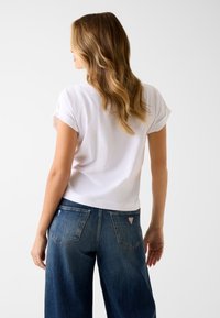 Wit T-shirt met korte mouwen en opgerolde manchetten, gecombineerd met een blauw denim jeans met hoge taille, achterzakken en een klein logoplaatje.