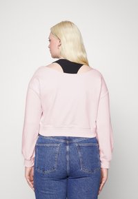 Sweatshirt cropped rosa com mangas longas, apresentando um detalhe de decote largo. Combinado com jeans de denim azul de cintura alta com bolsos traseiros.