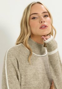 Maglione girocollo beige in morbido tessuto a maglia, con colletto e polsini a coste rifiniti con dettagli in bianco lungo le spalle.
