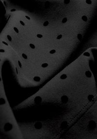 Čierna tkanina s roztrúsenými čiernymi bodkami. Mäkka textura s hladkým povrchom, znázorňujúc jemné záhyby a švy.