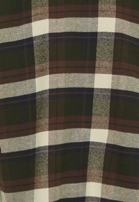 Tkanina w kratę z białymi, ciemnozielonymi, burgundowymi i granatowymi wzorami. Tekstura wydaje się tkana, z miękkim, lekko chropowatym wykończeniem.