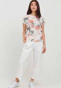 Top floral de manga corta en crema con patrones en rosa y verde, combinado con pantalones anchos blancos y zapatillas blancas.