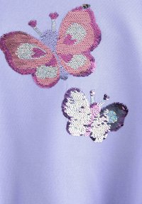 Lilla stof har to paliet-broderede sommerfugleapplikationer; en pink og en flerfarvet med iriserende accenter og indviklede detaljer.