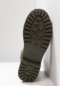 Zelená gumová podrážka boty s hlubokým vzorem pro trakci, obsahující '+' tvary a vyvýšené logo značky. Pevný design s texturovaným povrchem.