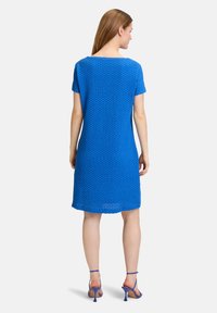 Blaues gestricktes Kleid mit kurzen Ärmeln, rundem Ausschnitt und mittellanger Länge. Besitzen ein strukturiertes Muster und wird mit passenden blauen Absatzsandalen getragen.