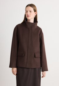 Hnědá bunda z vlna-směsi s vysokým límcem, dvěma předními kapsami, strukturovanými rameny a čistým, minimalistickým designem.