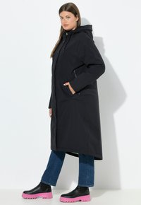 Dlouhý černý kabát s kapucí, s kapsami na zip. V kombinaci s tmavě modrými džíny a černými kotníkovými botami s růžovými podrážkami.