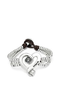 Pulsera de tono plateado que presenta un charm en forma de corazón con una piedra gris, hebras de cuentas y acentos de cuero marrón.