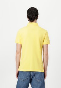 Gelbes Poloshirt mit klassischem Kragen und kurzen Ärmeln, aus weichem Stoff gefertigt. Die Rückseite hat ein einfaches Design und einen lässigen Schnitt.