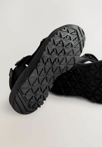 Svarta sandaler med en strukturerad gummisula med geometriska mönster. Justerbara remmar med en slät yta som betonar komfort och grepp.