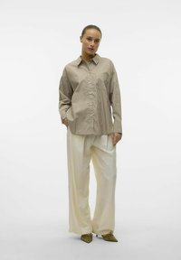 Skjorte med knapper i lys brun og kremfargede striper, kombinert med løse kremfargede bukser. Teksturert stoff, krage og detaljer med frontlomme.