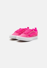 Zapatillas de ante rosa con cordones planos, suela de goma y una franja lateral en contraste. El diseño incluye una pestaña trasera para facilitar su uso.