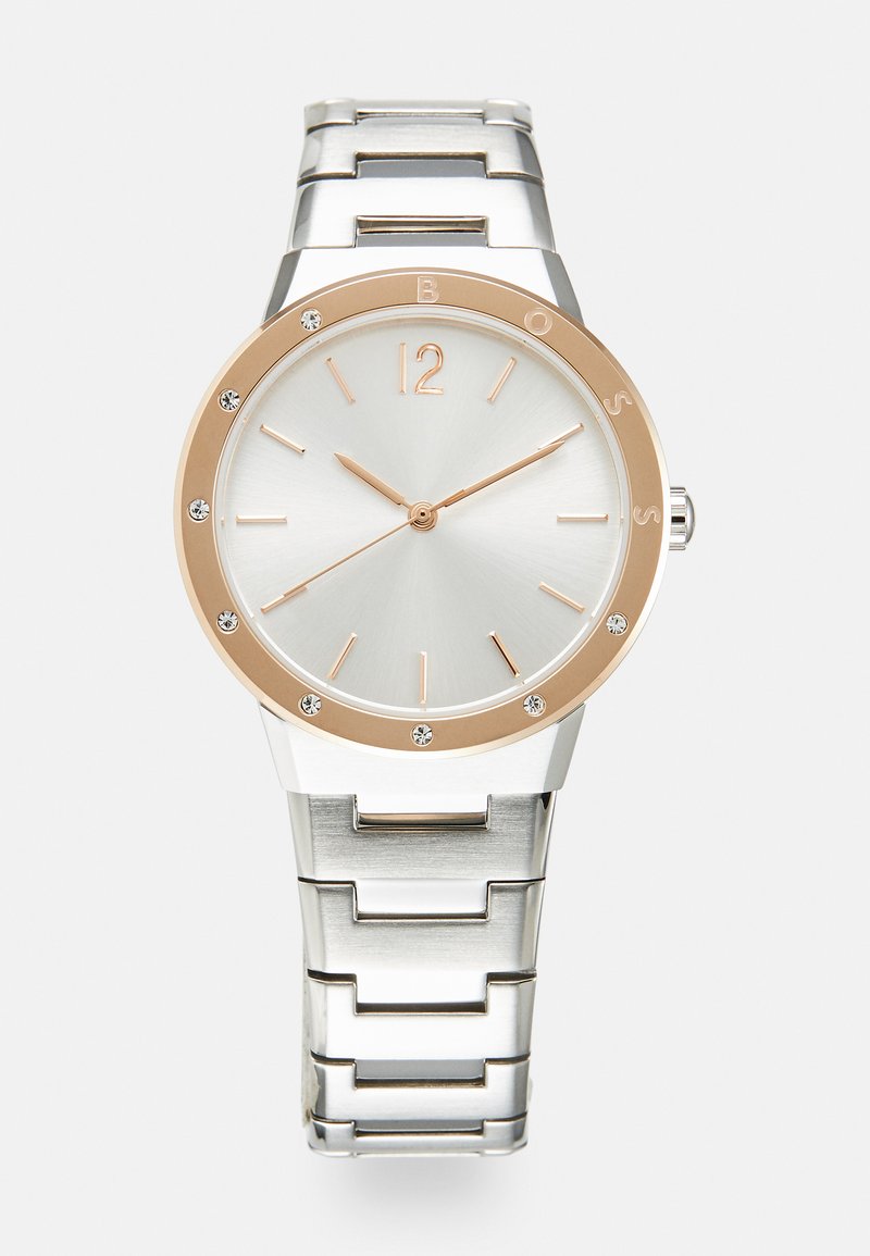 Reloj de acero inoxidable plateado con superficie pulida, bisel de oro rosa, esfera blanca, marcadores de horas dorados y acentos de cristal alrededor de la carátula.