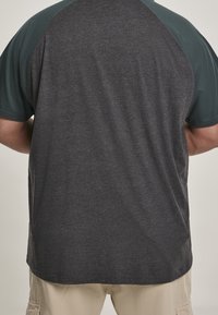 Koszulka z krótkim rękawem z ciemnoszarym korpusem i turkusowymi rękawami raglanowymi, wykonana z miękkiego materiału o gładkiej fakturze, o luźnym kroju.