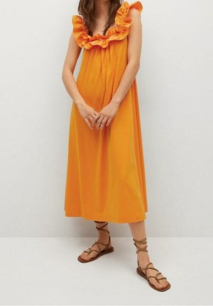 Robe en coton orange avec encolure à volants, coupe au genou et coupe décontractée. Associée à des sandales marron à brides.