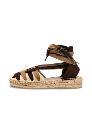 Sandalia espadrille plana en marrón y beige con tiras de tela y cierre de tobillo sobre suela de yute trenzado.