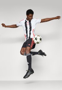 White and black striped soccer jersey with red accents, black shorts, black soccer cleats, and black and white soccer ball featuring green stars.
