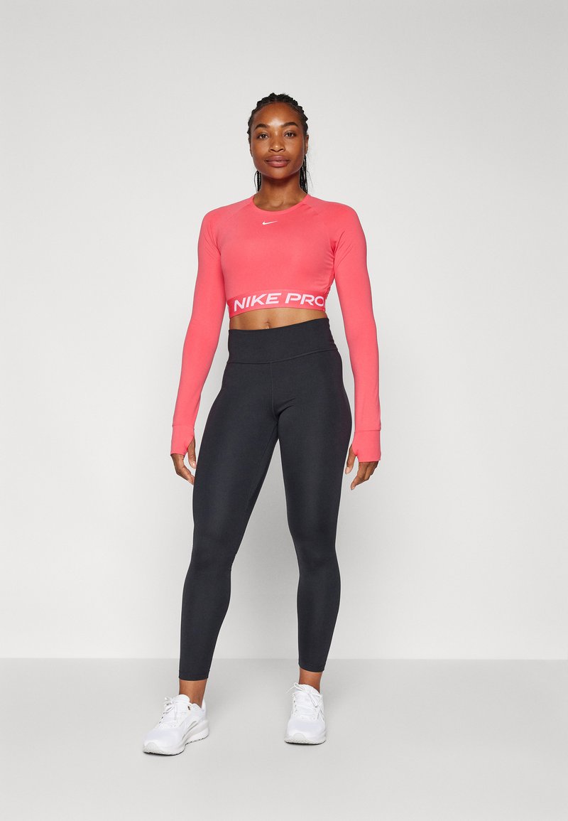 Czarny długi rękawowy top Nike Pro w jaskrawym różowym kolorze z białym logo, zestawiony z czarnymi legginsami z wysokim stanem i białymi butami sportowymi.