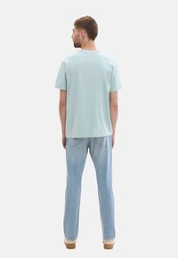 Helles blaues T-Shirt mit kurzen Ärmeln, lockere Passform, aus Baumwolle, schlichtes Design. Kombiniert mit hellblauen Jeans und braunen Schuhen.