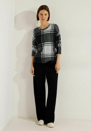 Black and white plaid sweater with long sleeves, round neckline, and drop shoulders, paired with loose black trousers and white sneakers.