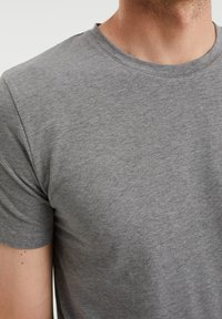 Camiseta de algodón gris de cuello redondo con un acabado suave y mangas cortas. La tela tiene un ligero jaspeado y un ajuste casual.