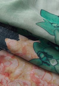 Tessuto con motivo floreale nei toni del verde, rosa e crema, caratterizzato da una texture morbida con pieghe stratificate e lisce.