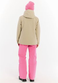 Beige waterdichte jas met een capuchon en roze sneeuwbroek. De outfit heeft een gladde textuur en is gecombineerd met zwarte buitenschoenen.