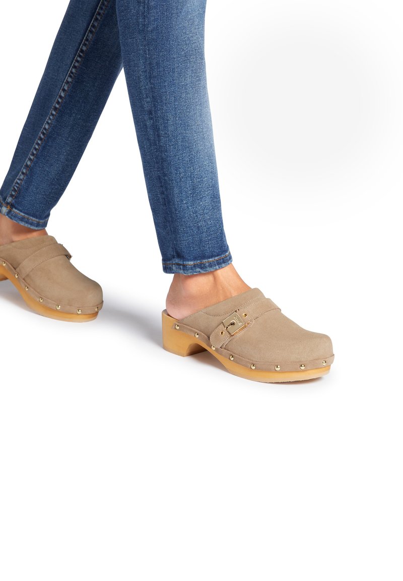 Beige suède klompen met houten zolen, voorzien van een gespsluiting en gouden studs langs de randen. Gekocht met blauwe spijkerbroeken.