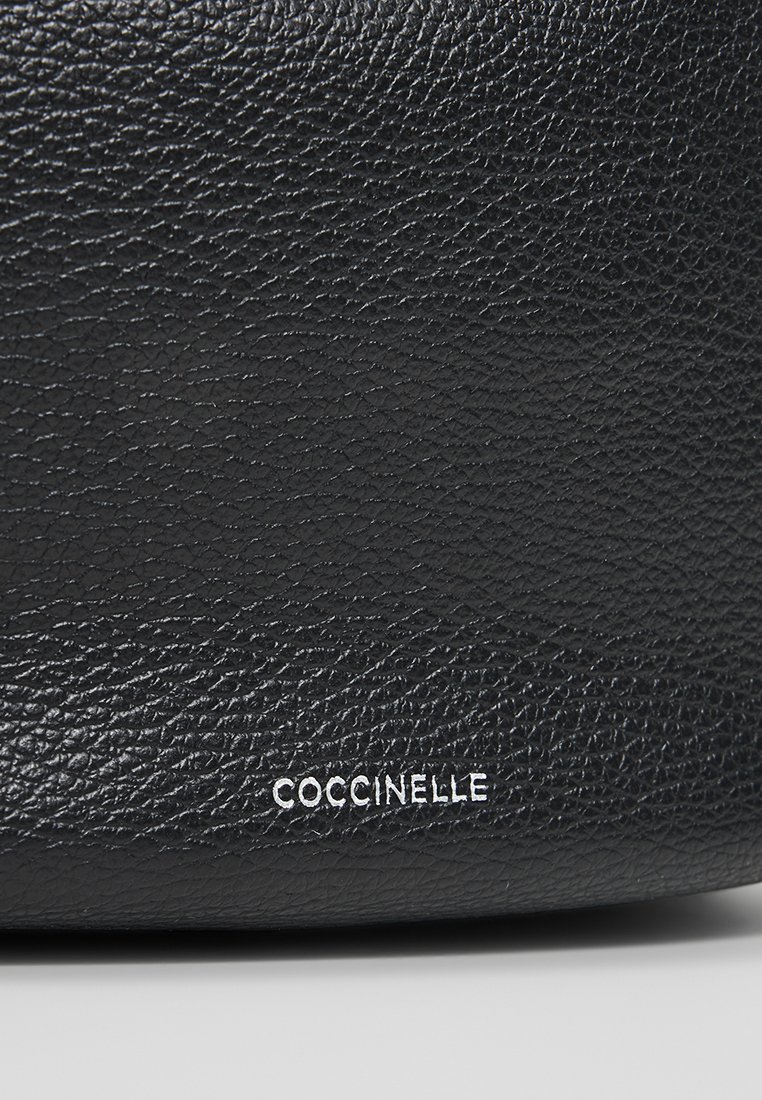 Sac à main en cuir noir avec une surface texturée et le logo embossé "COCCINELLE" en blanc. Il présente un design élégant et minimaliste.