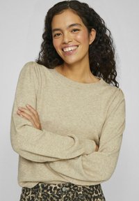 Beige krēmo džemperis ar apaļu kakla izgriezumu, teksturētu adījumu un gumijotām piedurknēm. Savairots ar leopardu raksta augsto vidukli biksēm.