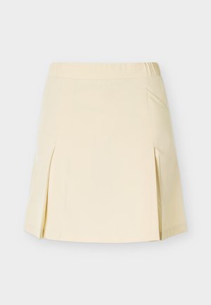 Μπεζ φούστα μέχρι το γόνατο με πτυχώσεις στο πλάι και ελαστική μέση, σε απλό φωτεινό φόντο.