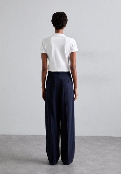 White cotton polo shirt and dark navy wide-leg trousers with two back pockets, featuring subtle stitching details on the waistband.
