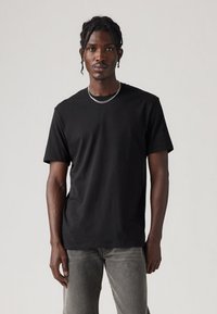 Juoda medvilninė trumparankovė marškinėliai su apvalia iškirpte. Dėvimi su pilkais džinsiniais kelnėmis; lygi tekstūra su minimaliais dizaino elementais.