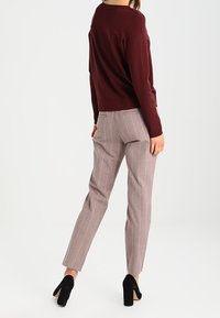 Pull bordeaux à coupe décontractée, associé à un pantalon rayé gris clair. Des talons noirs complètent la tenue, soulignant le look soigné.