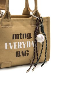 Khaki-Leinwand-Tote mit dem Aufdruck "mtng. EVERYDAY BAG" in Braun und Weiß. Verfügt über geknotete Schnüre und einen kleinen baseballförmigen Anhänger.