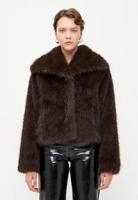 Pruun faux-fur lühike jakk, millel on salli krae, pikad varrukad ja pehme tekstuur; koos läikivate mustade rõngavarrukatega pükstega.
