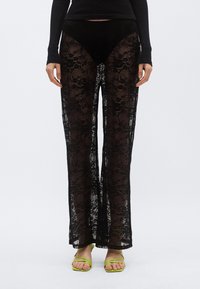 Mustad pitspüksid, millel on voolav, läbipaistev disain lillemustritega. Kaasaitud roheliste rihmikandadega sandaalid.