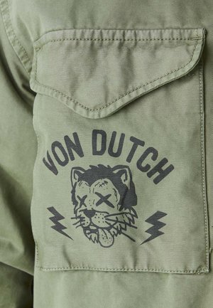 Poche en tissu vert avec un graphisme noir d'une tête de tigre dessin animé aux yeux barrés et langue tirée, texte "VON DUTCH" au-dessus et éclairs en dessous.