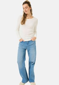 Maglietta bianca a maniche lunghe con scollo rotondo abbinata a jeans a gamba larga di un blu chiaro, caratterizzati da una vestibilità rilassata e tasche frontali.