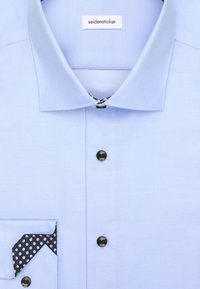 Lichtblauw overhemd met een gestructureerde kraag, zwarte knopen en een zak met een zwart-wit stippenpatroon.